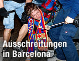 Ein Polizist mit Schlagstock h&auml;lt eine Person mit Barcelona-Schal fest.