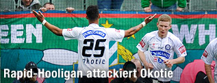 Rubin Okotie mit ausgebreiteten Armen vor der Rapid-Fantribüne