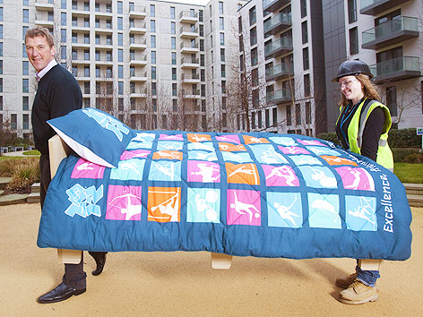 © APA/EPA/Dave Poultney Zwei Personen tragen ein Bett, der Olympiateilnehmer vor dem Olympischen Dorf in London