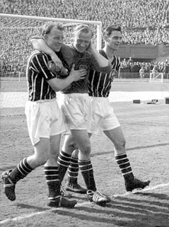 © AP Bernd Trautmann greift sich nach dem FA-Cup-Finale 1956 auf seinen Nacken und wird von zwei Teamkollegen gestützt