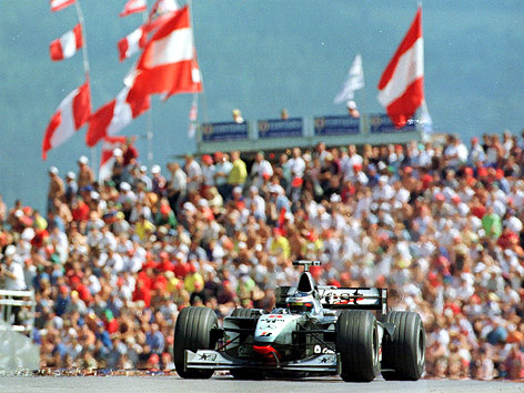 Mika Hakkinen im McLaren-Mercedes 1998 vor einer Zuschauertribüne mit zahlreichen Österreich-Fahnen